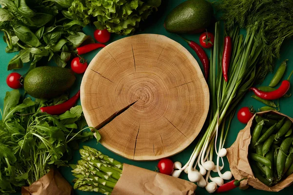 Vue de dessus de la coupe de bois entourée de différents légumes mûrs sur la surface verte — Photo de stock