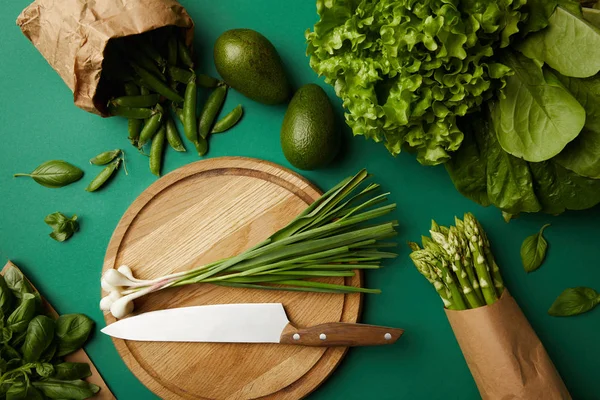 Vista superior de diferentes vegetais maduros com placa de corte de madeira e faca na superfície verde — Fotografia de Stock