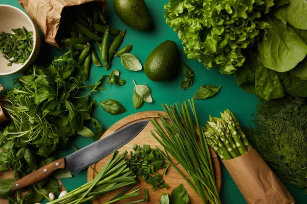 Vista superior de varias verduras maduras con tabla de cortar de madera y cuchillo en la superficie verde - foto de stock