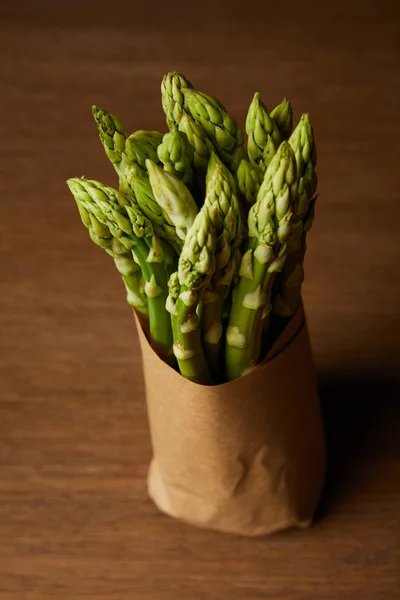 Close-up shot of bunch of asparagus covered with kraft paper on wooden surface — Stock Photo