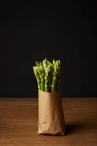 Close-up shot of bunch of ripe asparagus covered with kraft paper on wooden surface — Stock Photo