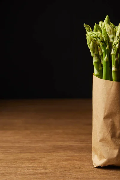 Cropped shot of bunch of ripe asparagus covered with kraft paper on wooden surface — Stock Photo