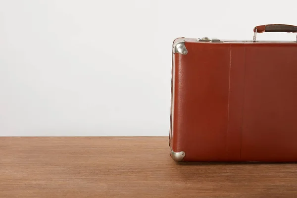 Vintage leather suitcase on wooden table by white wall — Stock Photo