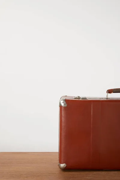 Brown vintage suitcase on wooden table by white wall — Stock Photo