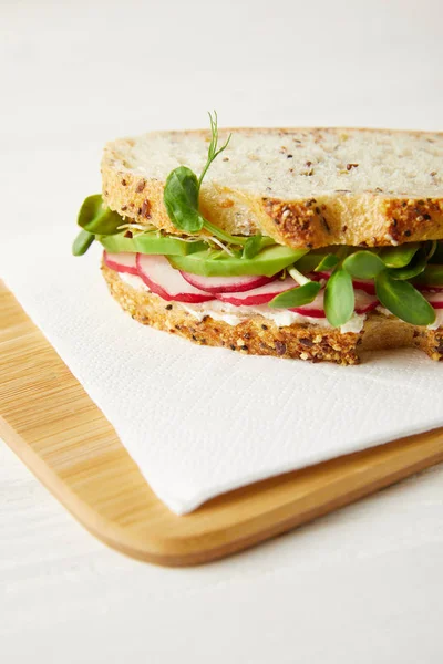 Primer plano de bocadillo fresco con rodajas de rábano, aguacate y brotes de guisantes en la tabla de cortar de madera - foto de stock