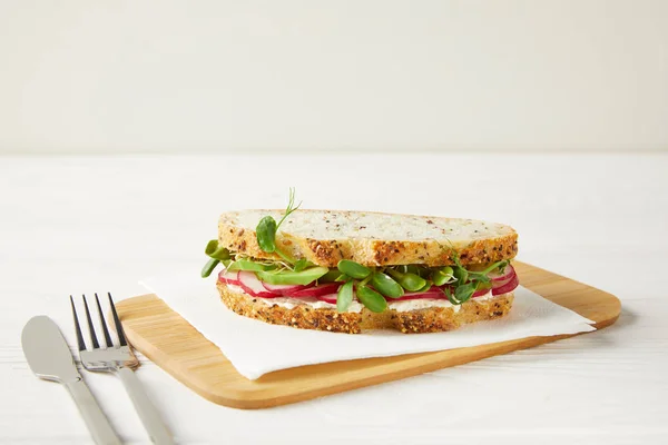 Delicioso sándwich con rodajas de rábano y brotes de guisantes en la tabla de cortar de madera - foto de stock