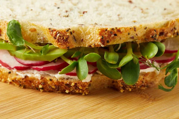 Primer plano de bocadillo vegetariano con rodajas de rábano y brotes de guisante en la superficie de madera - foto de stock