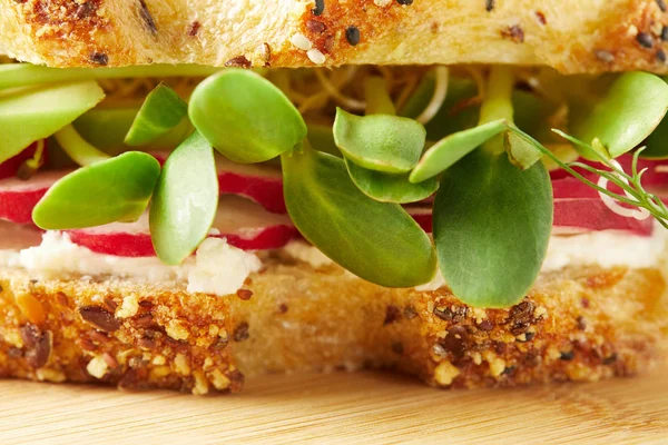 Primer plano de bocadillo saludable con rodajas de rábano y brotes de guisantes en la tabla de cortar de madera - foto de stock