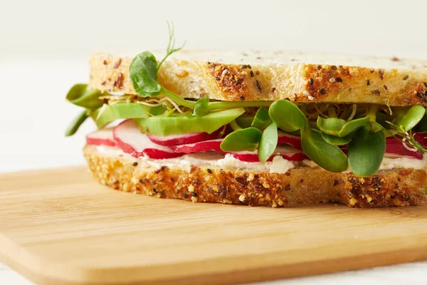 Tiro close-up de sanduíche saboroso com fatias de rabanete e brotos de ervilha na placa de corte de madeira — Fotografia de Stock