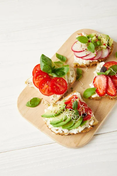 Various fresh sandwiches on cutting board and on white tabletop — Stock Photo