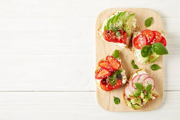 Top view of fresh sandwiches on cutting board on white wooden surface — Stock Photo