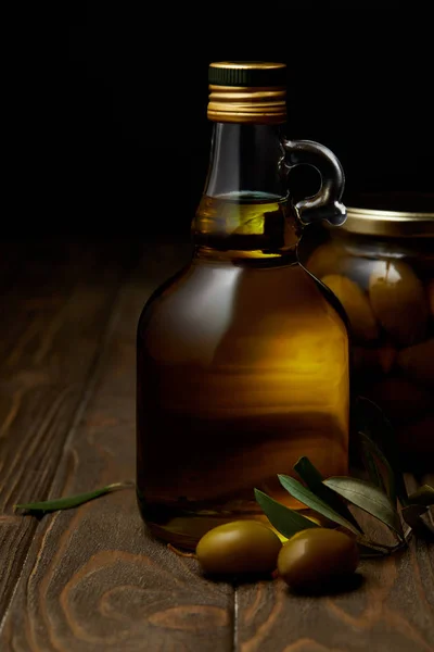 Botella de aceite de oliva aromático con rama y frasco sobre mesa de madera - foto de stock