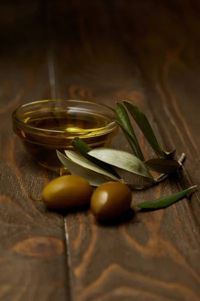 Close-up shot of olive oil with branch of olives on wooden surface — Stock Photo