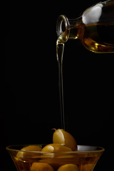 Aceite de oliva vertiendo en un tazón con aceitunas de botella aisladas en negro - foto de stock