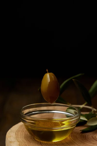 Reife Oliven fliegen über Schüssel mit Öl auf Holzbrett — Stockfoto