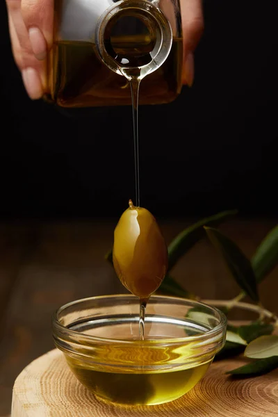 Colpo ritagliato di donna versando olio d'oliva in ciotola su tavola di legno — Foto stock