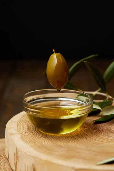 Azeite aromático pingando de oliveira acima da tigela em tábua de madeira — Fotografia de Stock