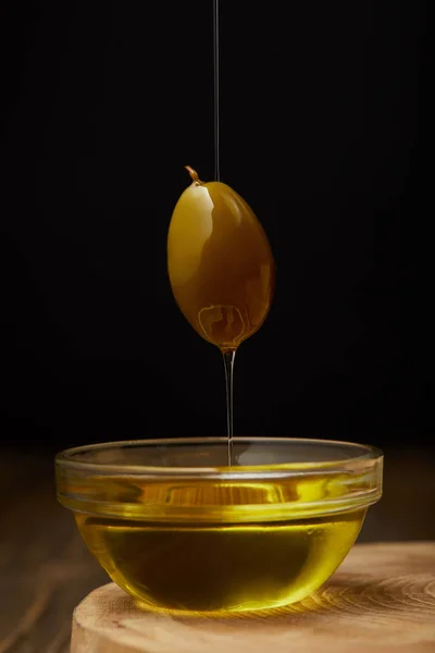 Fresh olive oil dripping from olive fruit above bowl on wooden surface — Stock Photo