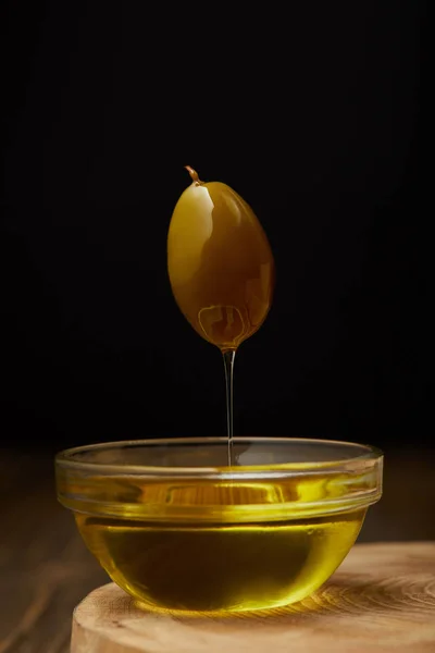 Azeite de oliva pingando de oliveira acima da tigela na superfície de madeira — Fotografia de Stock