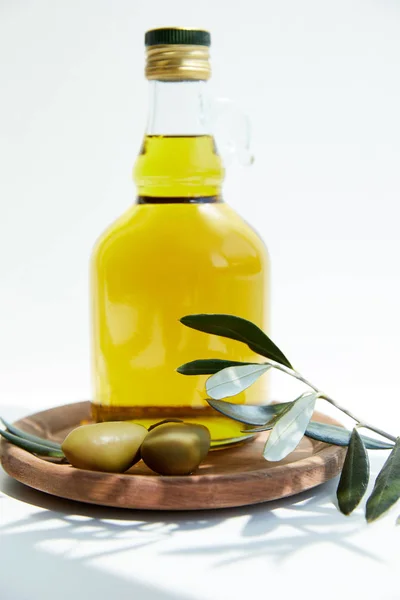 Bottle with aromatic oil with green olives on wooden board with branch on white table — Stock Photo