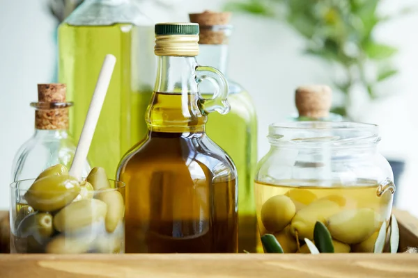 Verre avec cuillère et olives vertes, bocal, diverses bouteilles d'huile d'olive aromatique et branches sur plateau en bois — Photo de stock