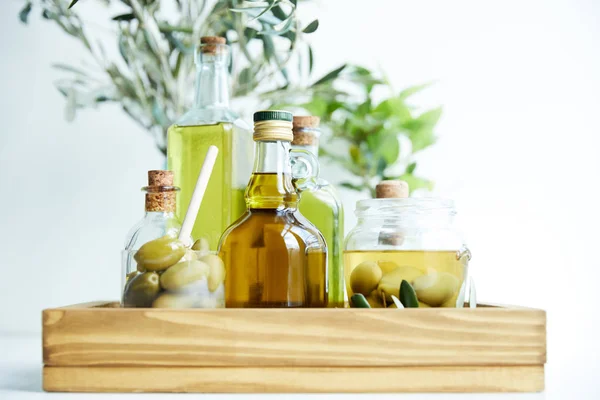 Verre avec cuillère et olives vertes, bocal, diverses bouteilles d'huile d'olive aromatique et branches sur plateau en bois — Photo de stock