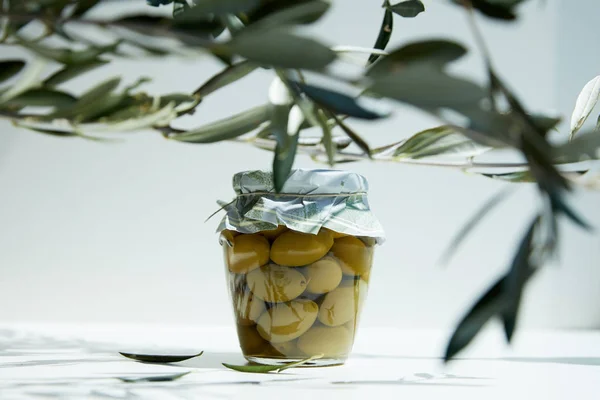 Glas aromatisches Öl mit grünen Oliven und Zweigen auf weißem Tisch — Stockfoto