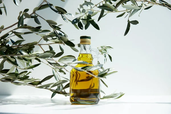 Botella de aceite de oliva aromático y ramas en la mesa blanca - foto de stock