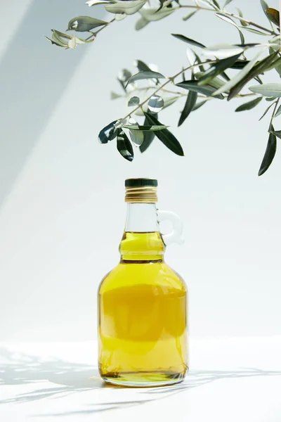 Vue rapprochée de bouteille d'huile d'olive aromatique et branches sur table blanche — Photo de stock