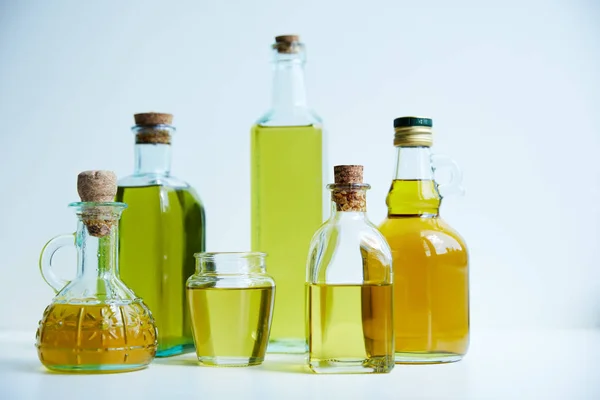Verschiedene Flaschen aromatisches Olivenöl und Glas auf weißem Hintergrund — Stockfoto