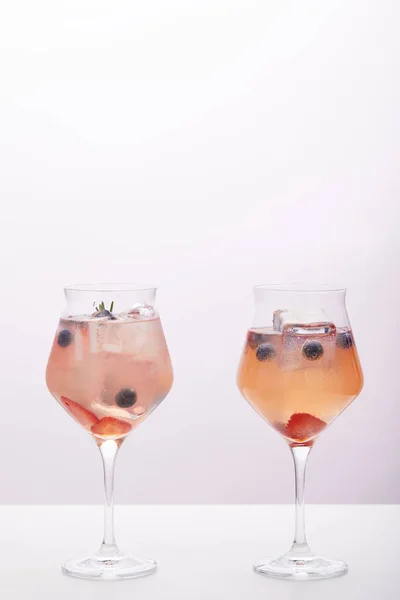 Two glasses of lemonade with ice cubes, rosemary, strawberries and blueberries isolated on grey background — Stock Photo