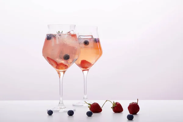 Dos vasos de limonada con cubitos de hielo, romero, fresas y arándanos aislados sobre fondo gris - foto de stock