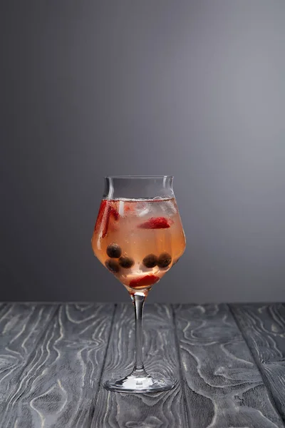 Glass of lemonade with ice cubes, blueberries and strawberries on grey background — Stock Photo