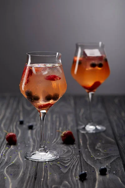 Two glasses of lemonade with ice cubes, strawberries and blueberries on grey background — Stock Photo