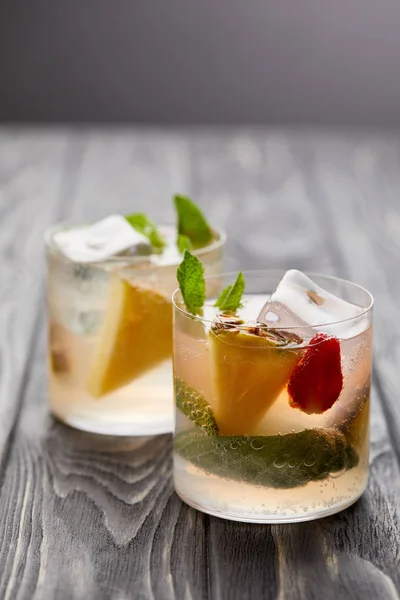 Two glasses of lemonade with ice cubes, mint leaves, pineapple pieces and strawberry — Stock Photo