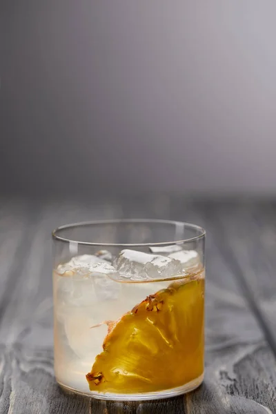 Glass of lemonade with pineapple piece and ice cubes on grey wooden table — Stock Photo