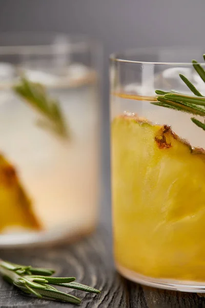 Gros plan de deux verres de limonade avec morceaux d'ananas, glaçons et romarin sur plateau en bois gris — Photo de stock