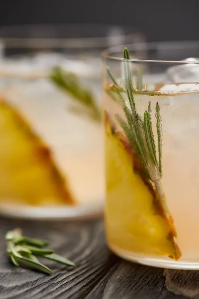 Imagen de cerca de dos vasos de limonada con trozos de piña, cubitos de hielo y romero sobre una mesa de madera gris - foto de stock