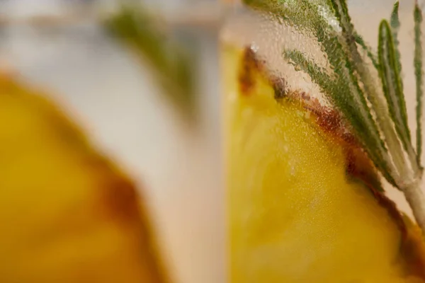 Selective focus of two glasses of lemonade with pineapple pieces, ice cubes and rosemary — Stock Photo