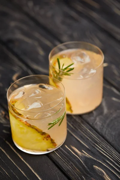 Dos vasos de limonada con trozos de piña, cubitos de hielo y romero sobre una mesa de madera gris - foto de stock