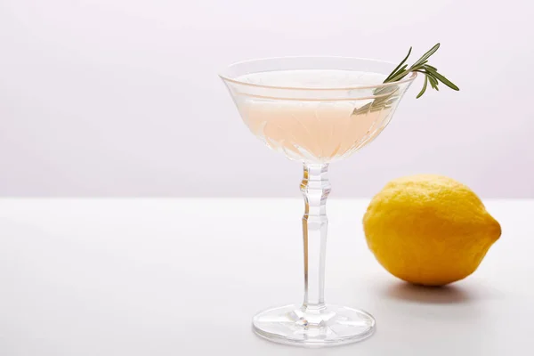 Glass of cocktail with rosemary and lemon on purple background — Stock Photo