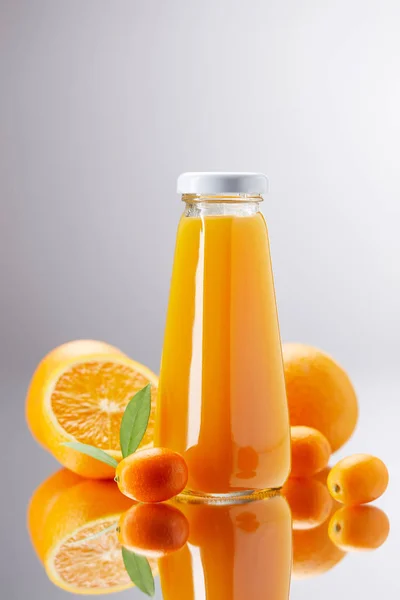 Bottle of fresh orange juice with oranges and kumquats on reflective surface — Stock Photo
