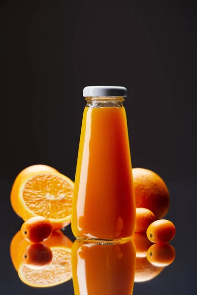 Botella de zumo de naranja fresco con naranjas y kumquats en superficie reflectante aislado en negro - foto de stock