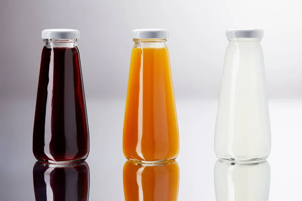 Rangée de bouteilles de jus divers sur surface réfléchissante — Photo de stock