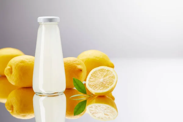 Botella de vidrio de limonada fresca con limones en superficie reflectante y en gris - foto de stock