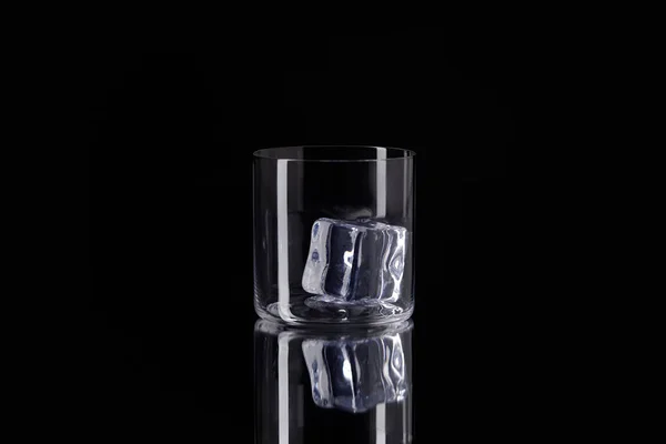 Vidrio con cubo de hielo en superficie reflectante aislado en negro - foto de stock