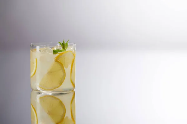 Single glass of fresh lemonade on reflective surface and on grey — Stock Photo
