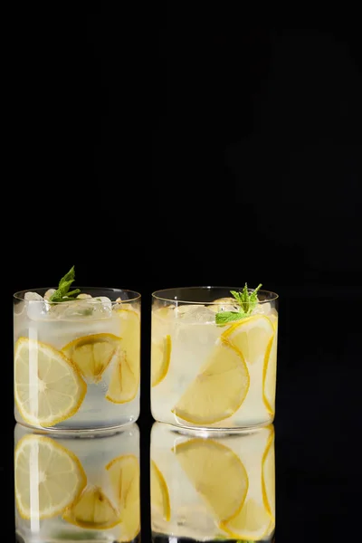 Glasses of delicious fresh lemonade on reflective surface isolated on black — Stock Photo