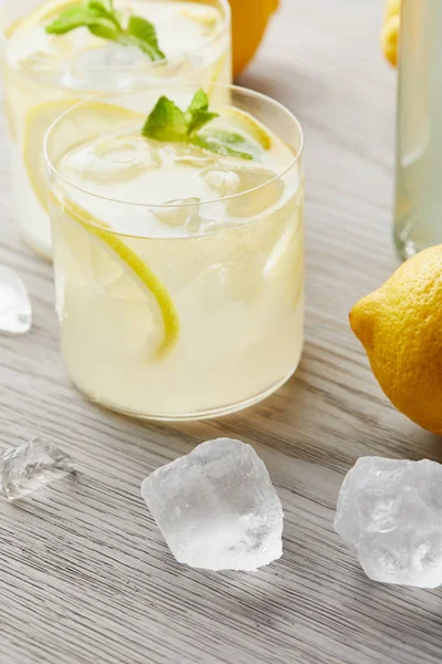 Close-up shot of fresh glasses of lemonade with ice and lemon on wooden surface — Stock Photo