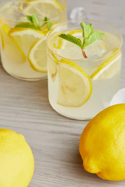 Primer plano de vasos de limonada con limones maduros en superficie de madera - foto de stock
